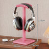 Pink headphone stand holding a pair of headphones on a wooden surface with measurements indicated.